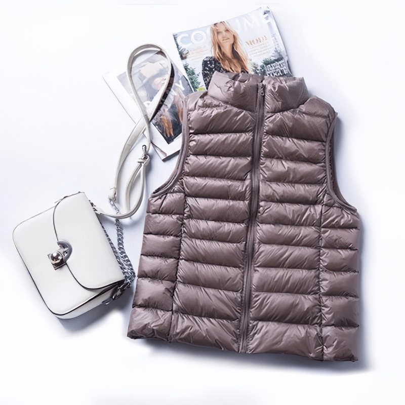 Women's windproof duck down vest with zipper and pockets, shown in a flat lay with a white crossbody bag and fashion magazine.